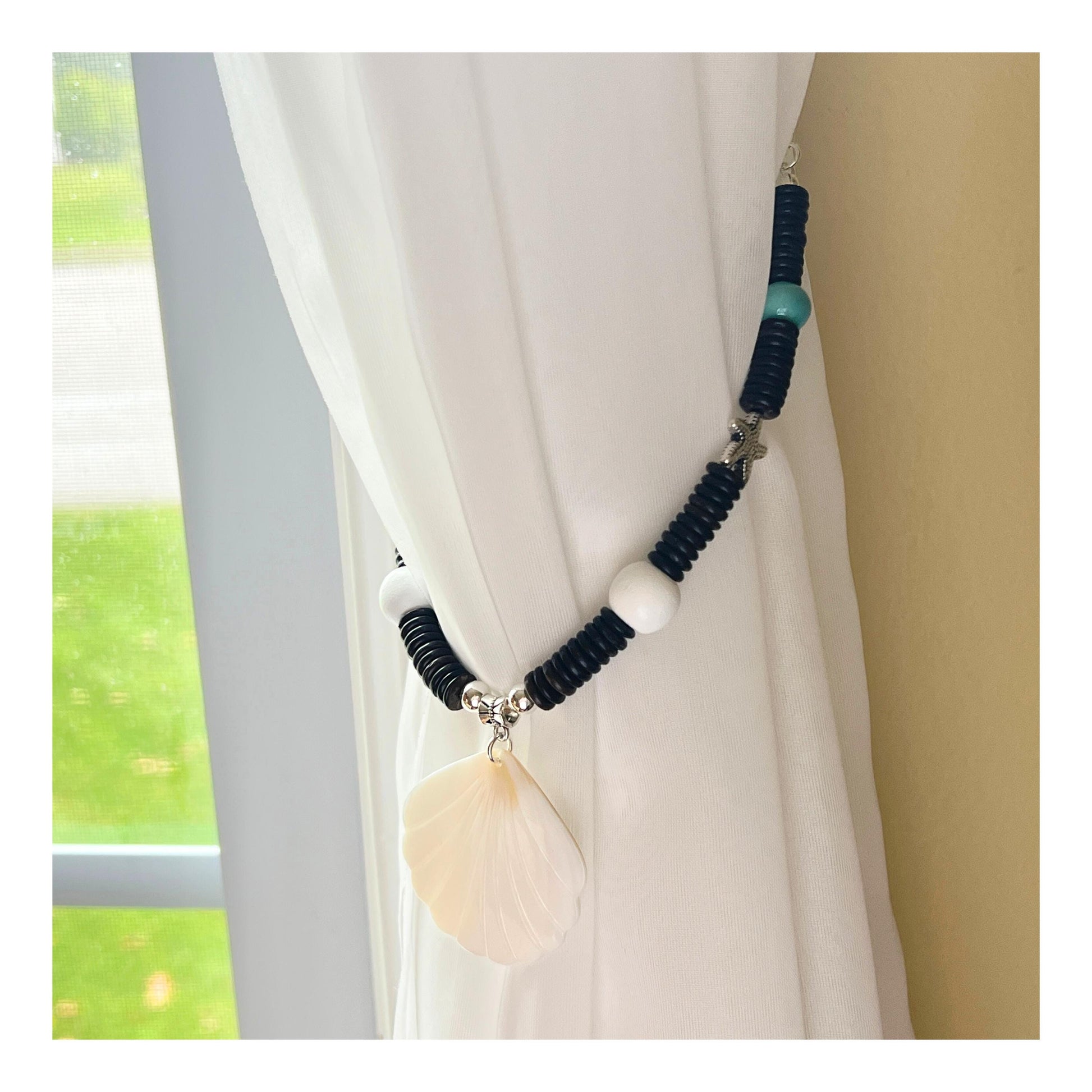 Set of two seashell and wood bead curtain tiebacks shown styled on sheer curtains — handmade coastal beach home decor
