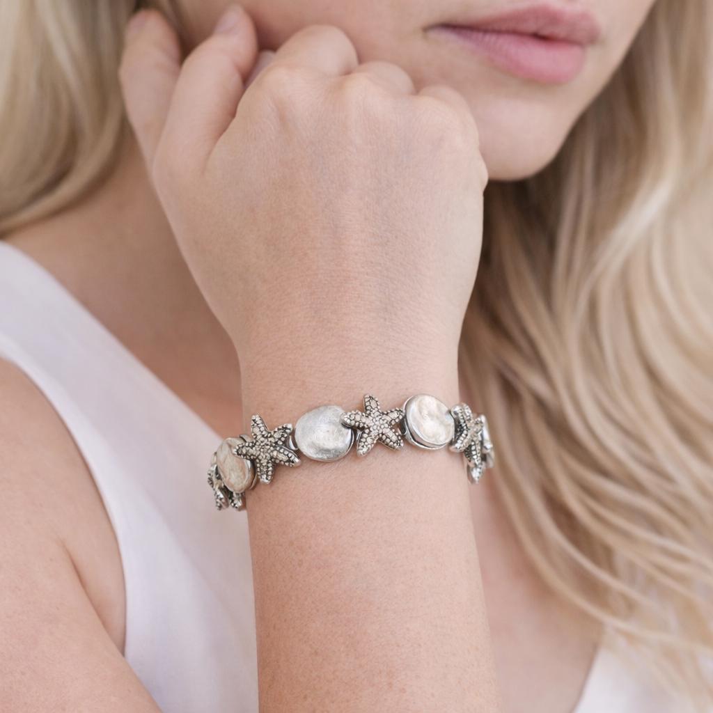 Seashell and starfish beach charm bracelet shown on a wrist — handmade coastal jewelry