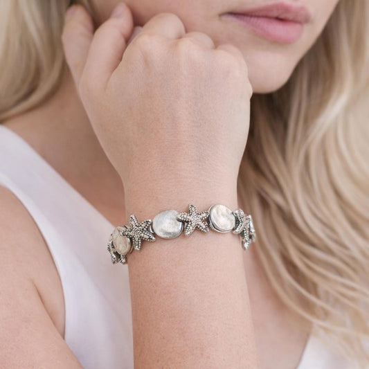 Seashell and starfish beach charm bracelet shown on a wrist — handmade coastal jewelry