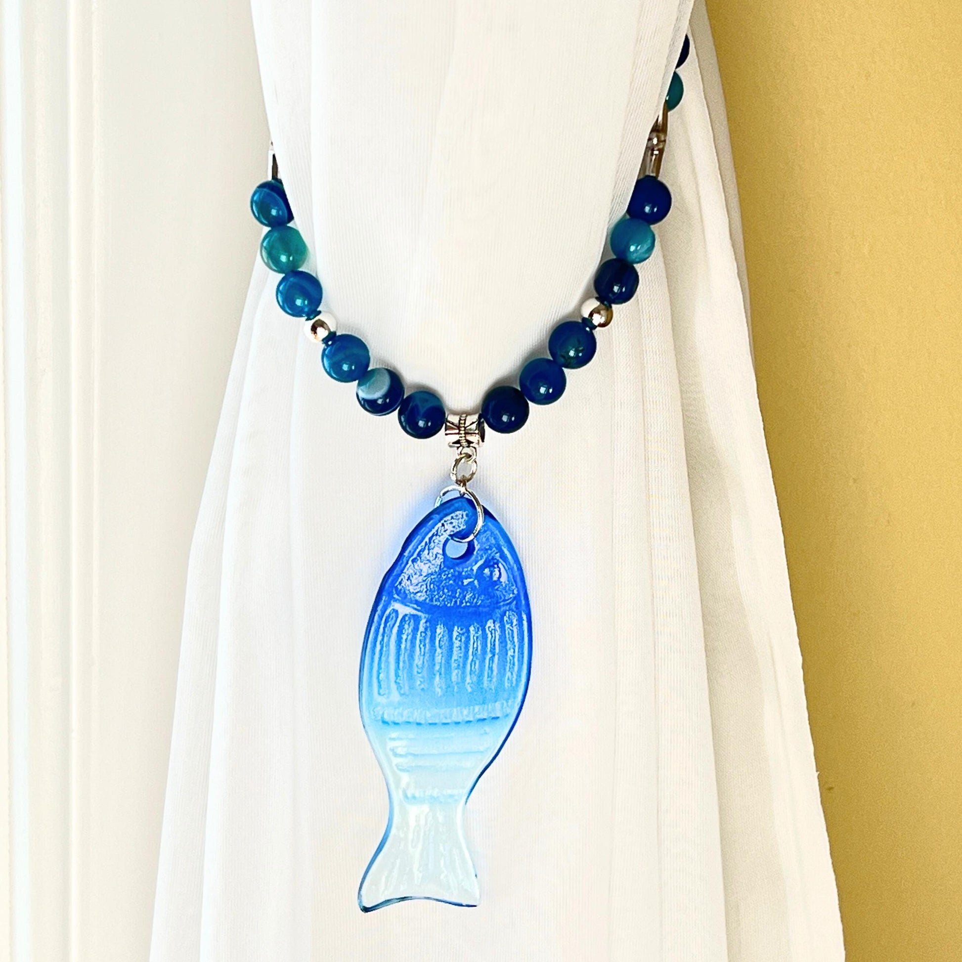 Blue glass fish curtain tiebacks shown styled on sheer curtains — handmade nautical beach home decor