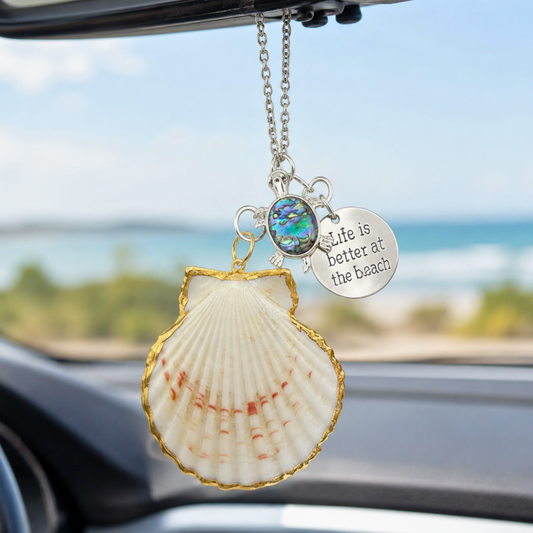 Shell-shaped car hanging ornament with 'Life is better at the beach' quote in a car interior.